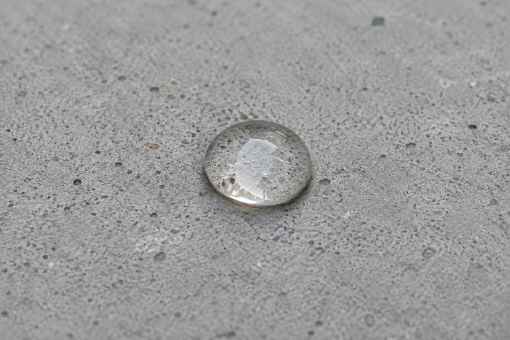 A close-up of a water droplet on a gray concrete surface.