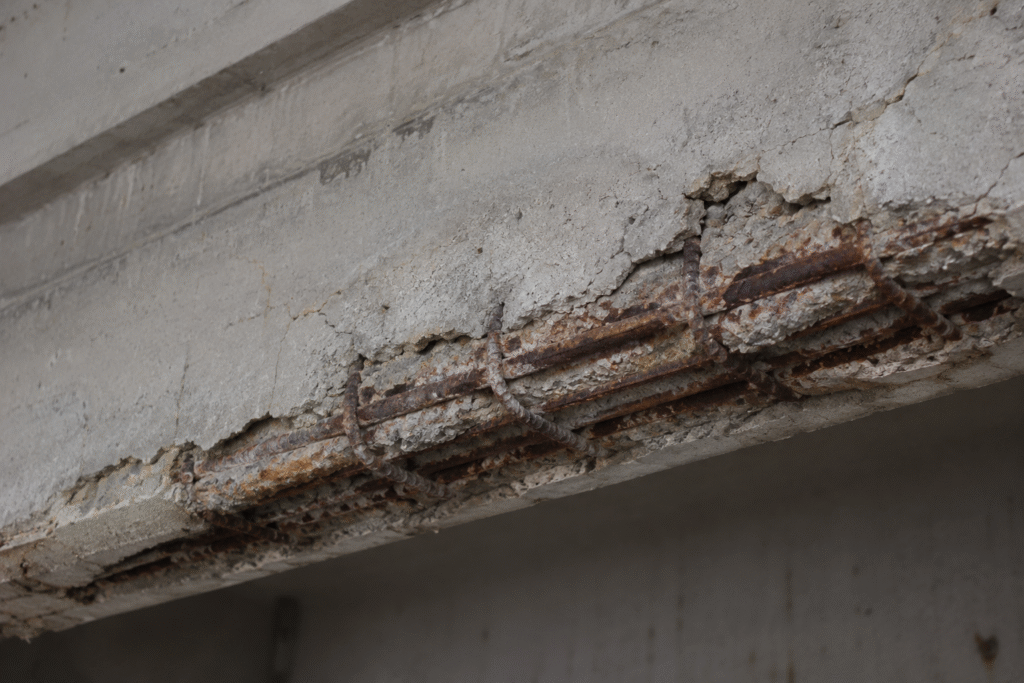 Corroded rebar exposed in a spalling and cracked concrete beam.